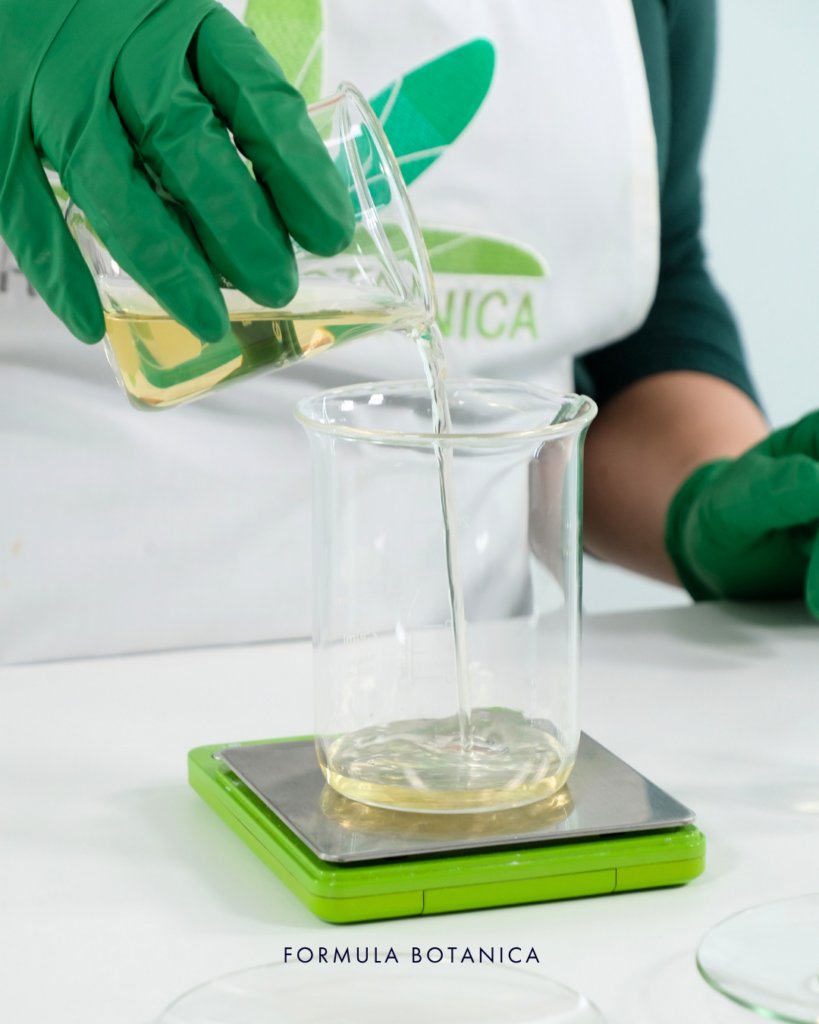 gloved hands showing step 1 of how to make a micellar water. Pouring ingredients into a beaker