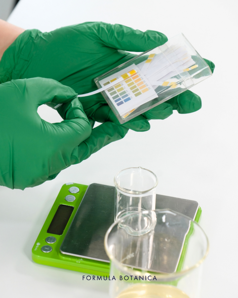 gloved hands showing step 3 of making a micellar water. Testing ph using strips